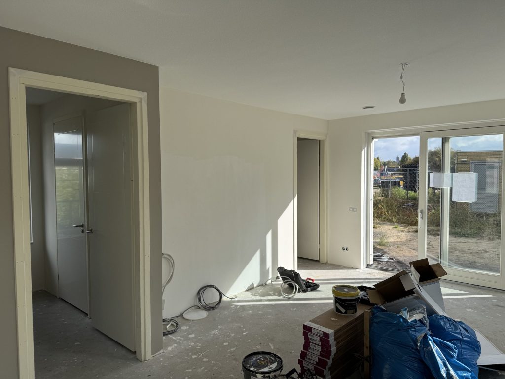 Nieuwbouwwoning in afwerking met lichte wanden, deuren naar de gang en materiaal op de betonvloer