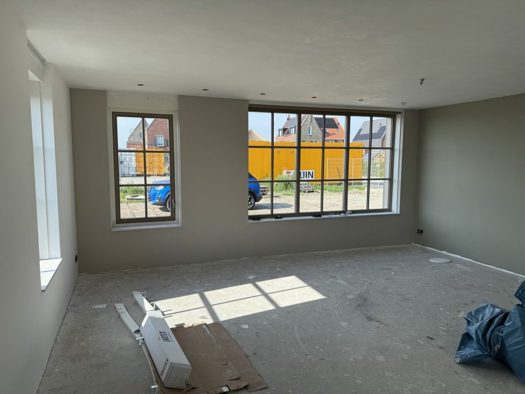 Nieuwbouwwoonkamer met wanden in warm grijs, een betonvloer en grote roedenramen