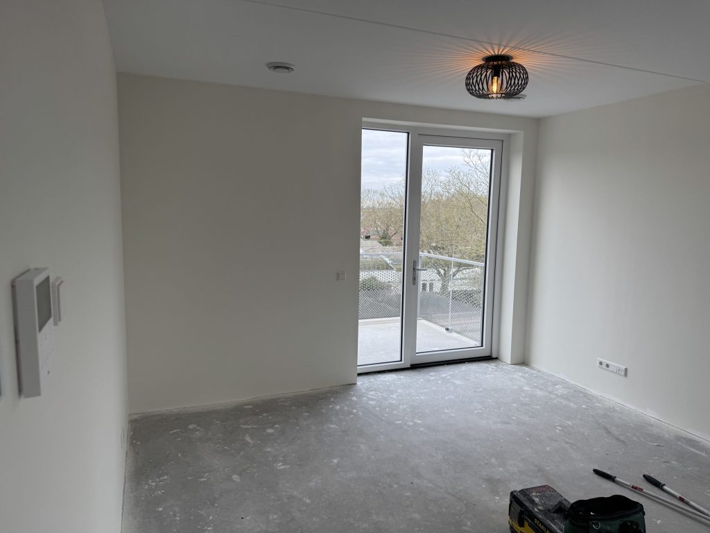 Lege kamer met strak witte wanden, een designlamp en openslaande deuren naar het balkon